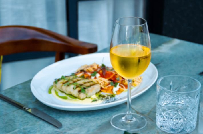 Na foto, uma mesa com um prato de comida e uma taça de vinho cheia - Metrópoles 